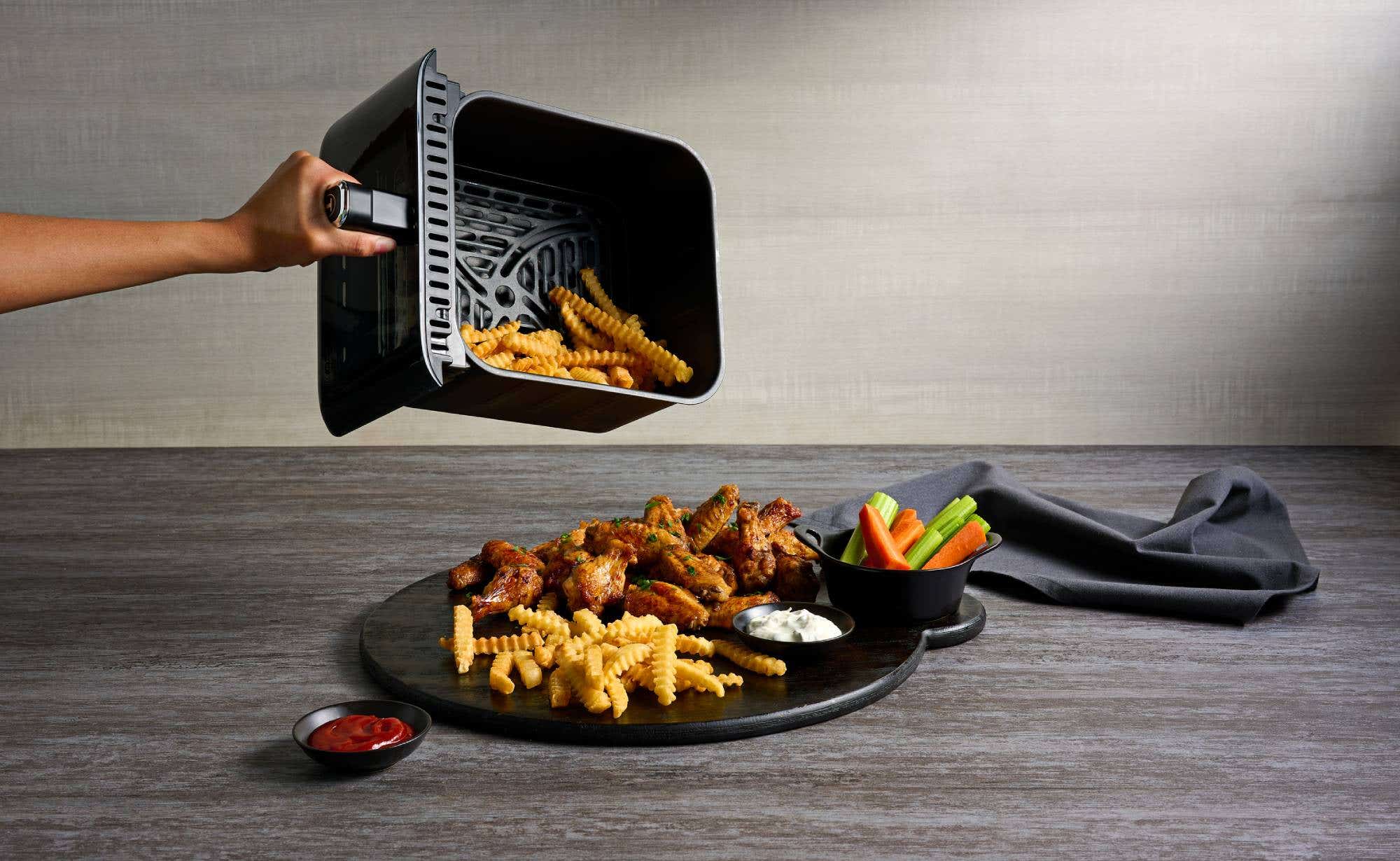 A person holds a tray air fryer's featuring a serving of fries and fresh carrots.